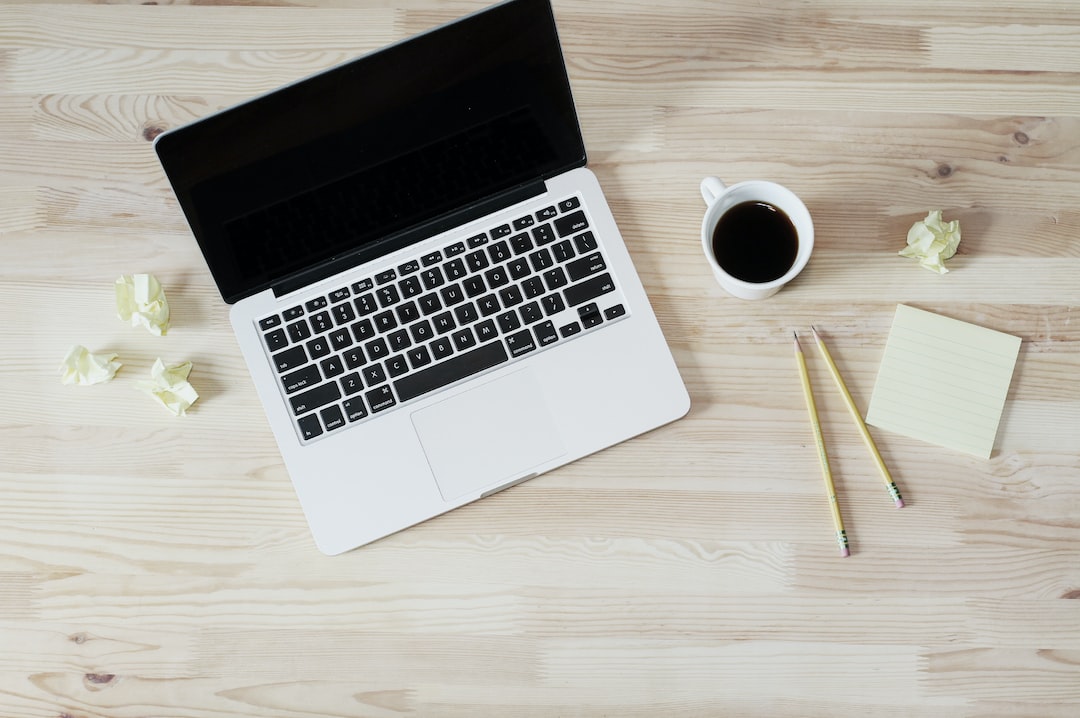A laptop on a light wooden desk with a cup of coffee, two yellow pencils, a pad of sticky notes, and a few crumpled paper balls scattered around—perfect for brainstorming your next WordPress Hosting project.