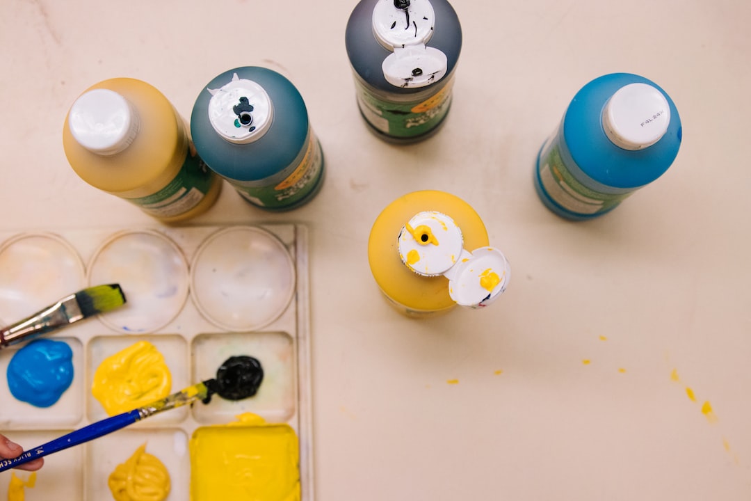 Bottles of yellow, blue, and green paint are arranged on a table next to a palette with paint wells, a paintbrush, blobs of yellow, blue, and black paint—creativity organized as expertly as quality WordPress Hosting.