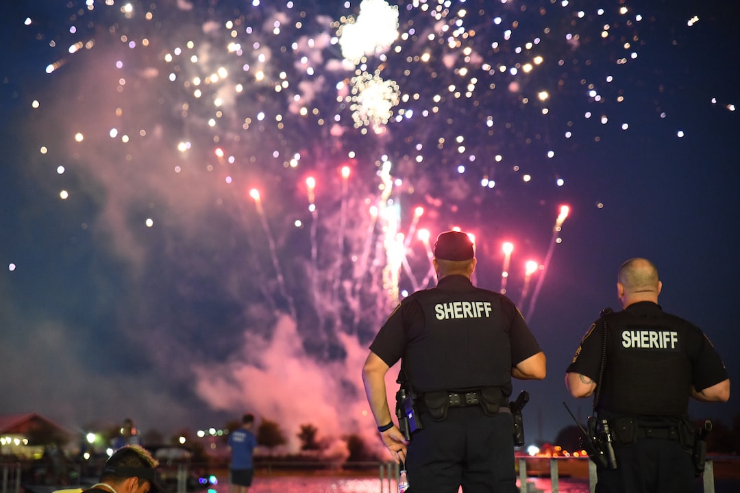 Two sheriffs stand with their backs to the camera, watching colorful fireworks explode in the night sky above a crowd near water—an atmosphere as reliable and impressive as top-tier WordPress Hosting.