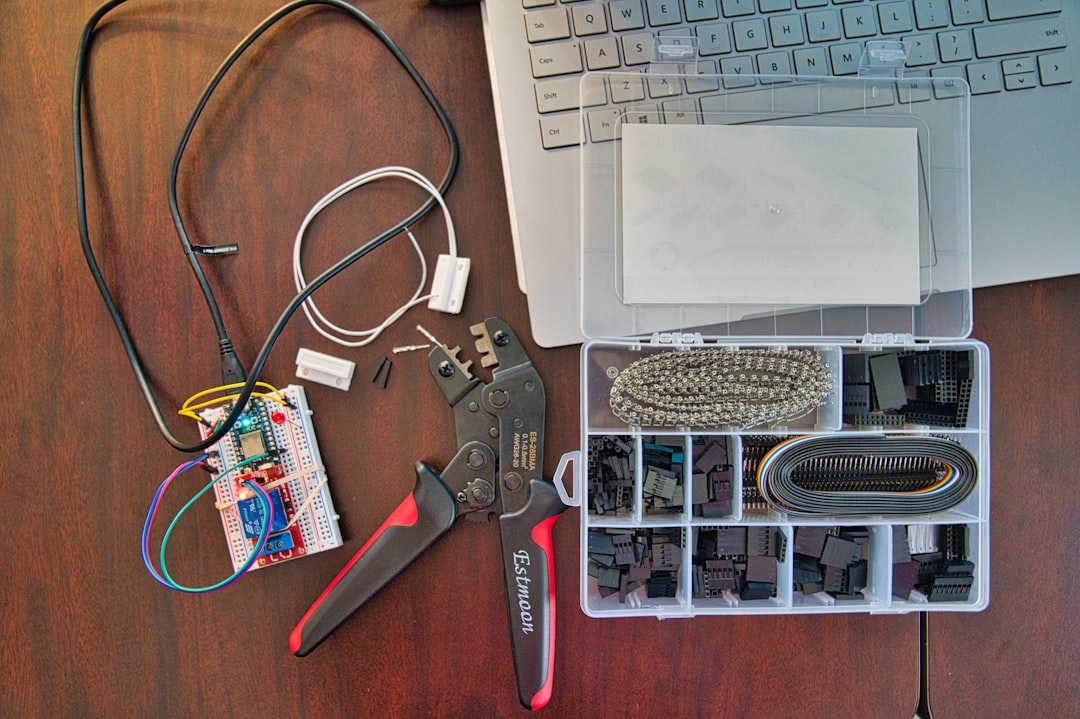 A breadboard with wires, a crimping tool, assorted connectors in a plastic box, and part of a laptop—ideal for tech setups or WordPress Hosting projects—are arranged on a wooden desk.