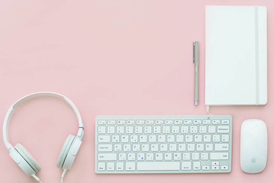 A flat lay of a white keyboard, mouse, headphones, pen, and closed notebook arranged neatly on a pastel pink background—perfect for planning your next WordPress Hosting project.