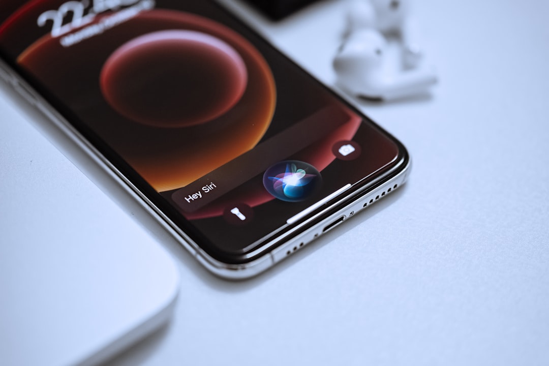A smartphone displaying the Siri interface with the “Hey Siri” prompt on screen, placed on a white surface next to a pair of wireless earbuds and a card advertising WordPress Hosting.