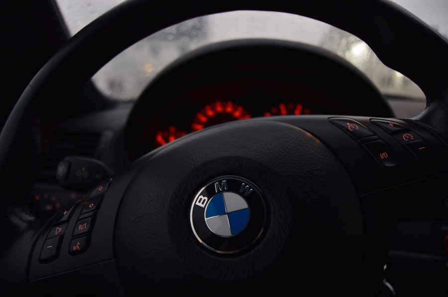 Close-up view of a BMW steering wheel inside a car, with the dashboard and illuminated red instrument panel in the background. The dim lighting draws attention to the BMW logo, much like premium WordPress Hosting highlights your website’s brand.